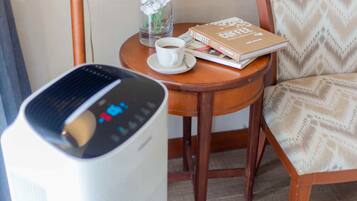 A room with a white air purifier, a small round wooden table with a white cup of coffee, a book, and a vase with white flowers.