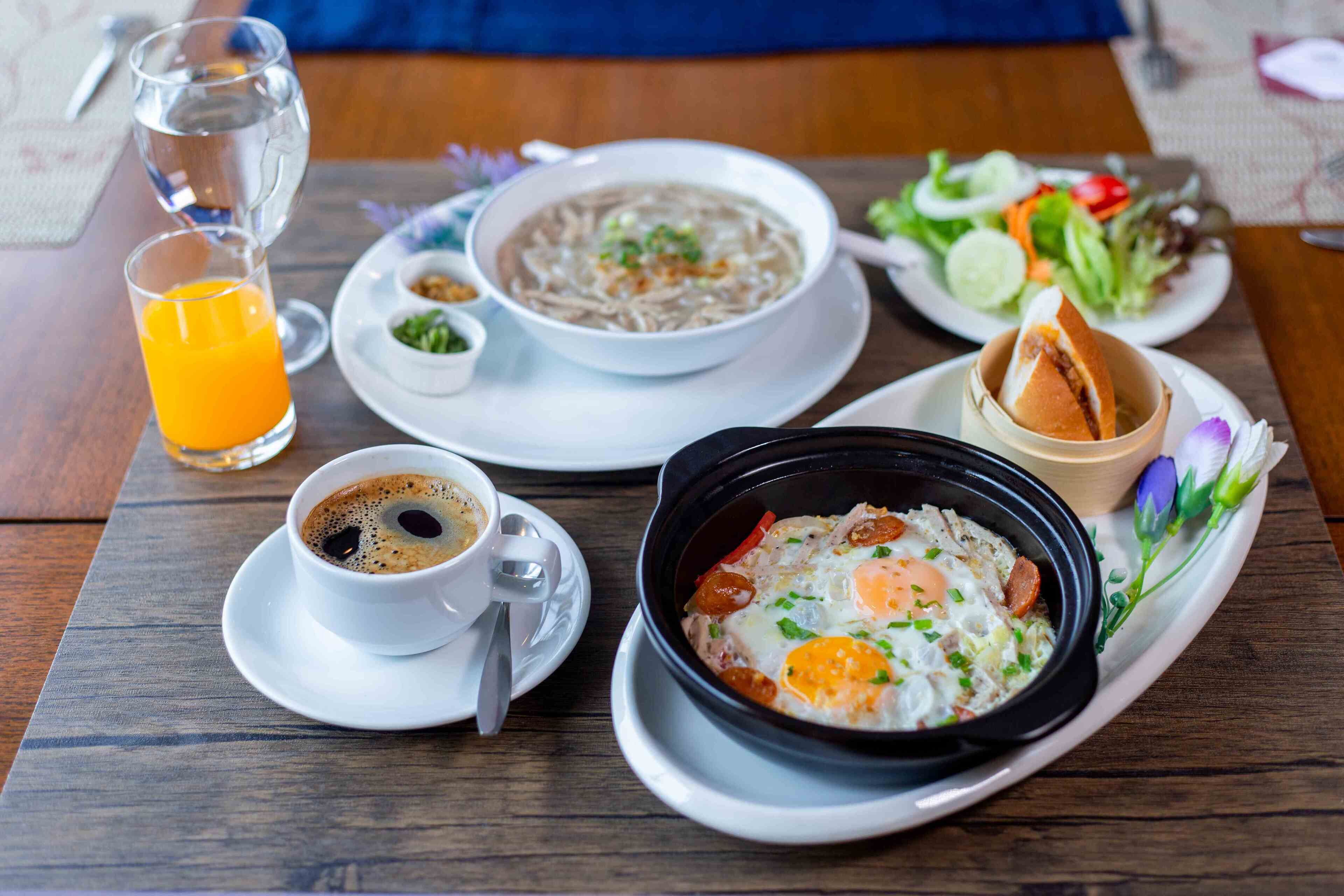 Une table en bois dressée pour le petit-déjeuner, avec un bol de soupe, une assiette d’œufs, un verre de jus d’orange et une tasse de café.