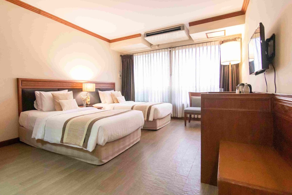 A hotel room with two beds, a desk, a chair, a TV, and a window with curtains.