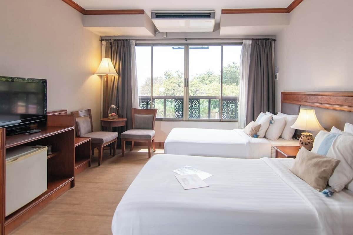 Habitación de hotel con dos camas, televisión, escritorio con lámpara y balcón con cortinas.