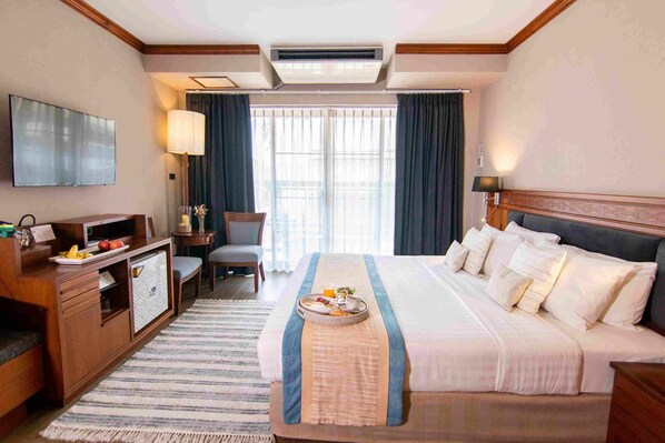 Ein Hotelzimmer mit einem großen Bett, einem Schreibtisch mit Flachbildfernseher, einem Sessel und einem Esstisch mit Frühstück.