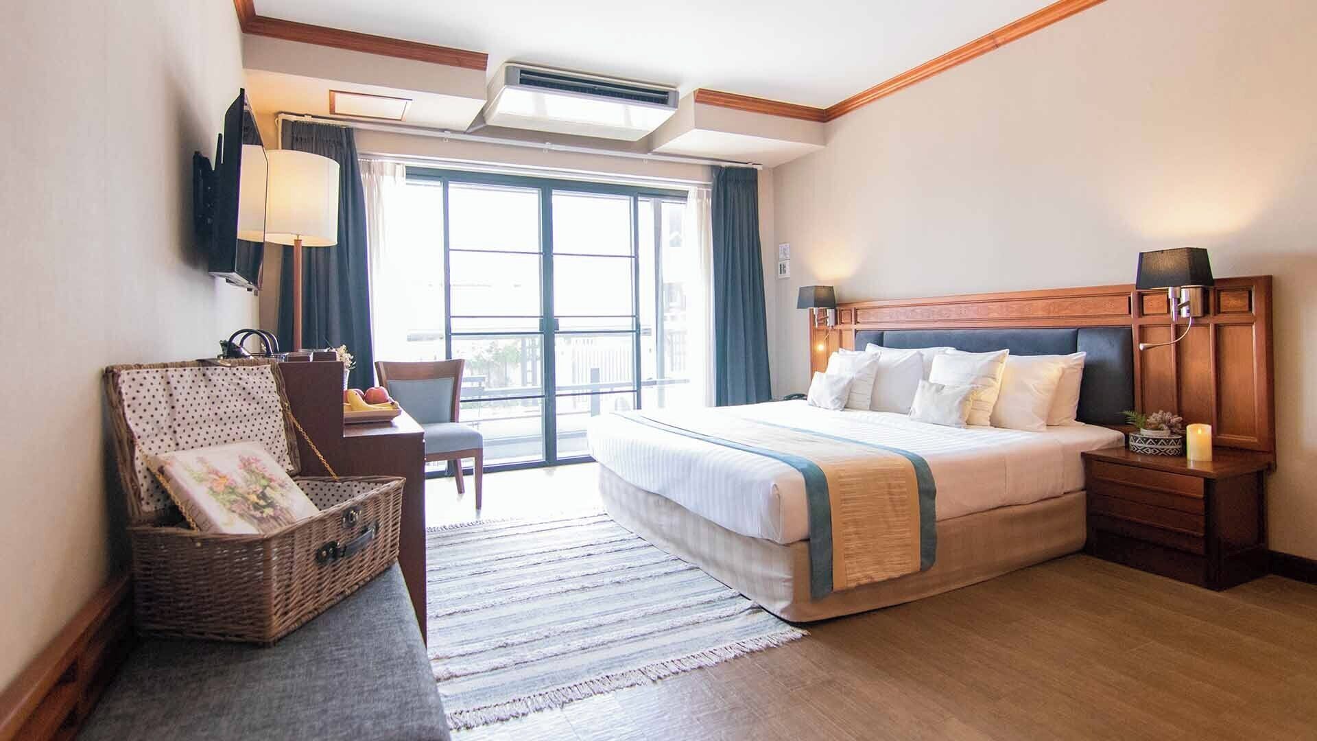 Una habitación de hotel con una cama grande, un escritorio con una silla, una cesta de mimbre y vistas al exterior a través de un ventanal.