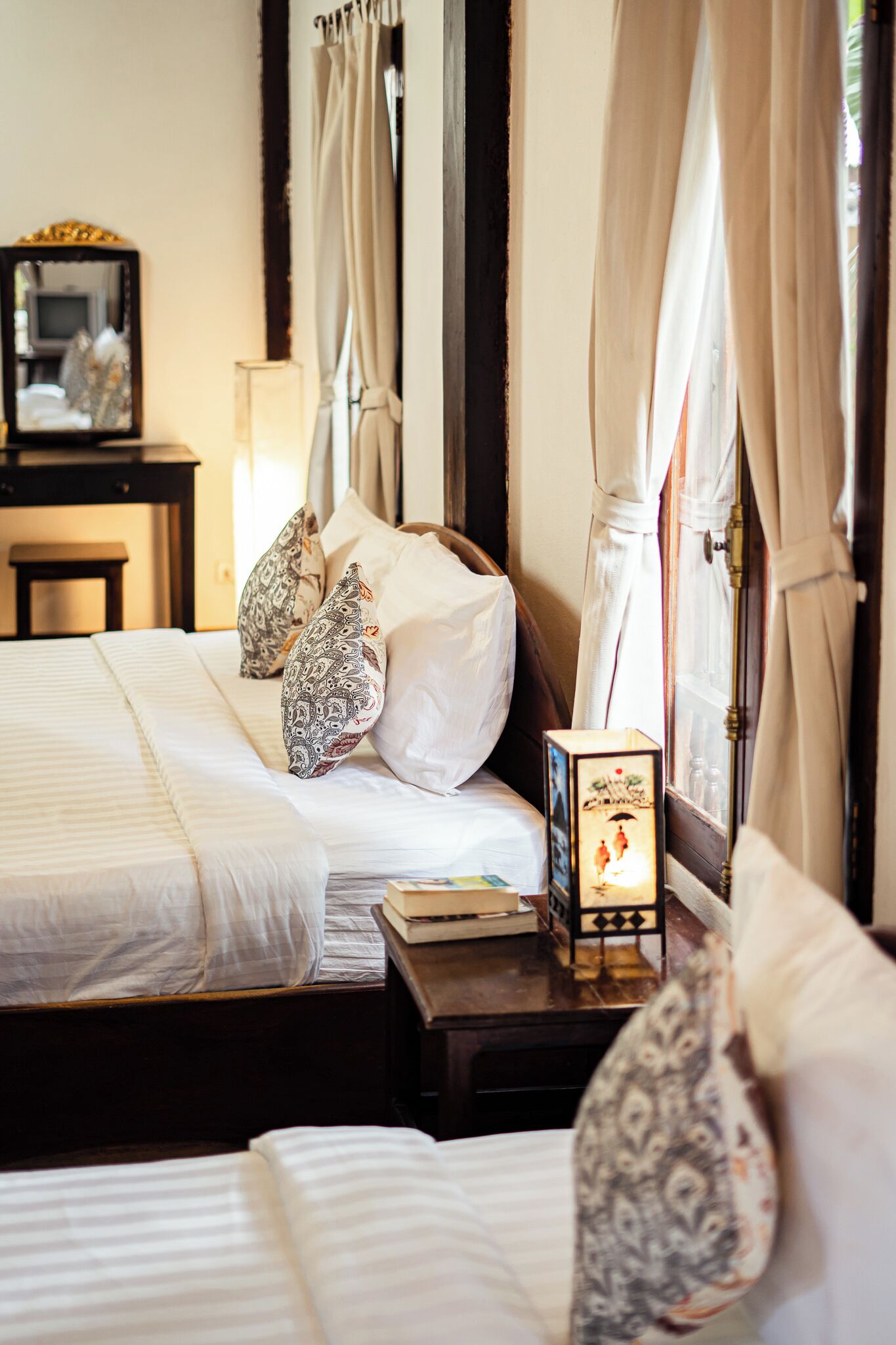 Een hotelkamer met twee bedden, een nachtkastje, een spiegel en een raam met gordijnen.