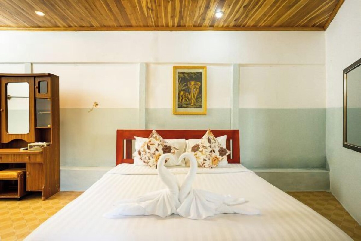 A hotel room with a bed, a wooden desk, a painting on the wall, and a large mirror.