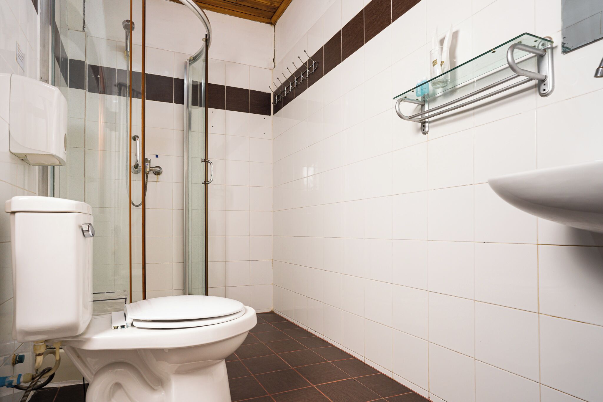 Une salle de bain équipée de toilettes, d’une douche et d’une étagère en verre où sont rangés les articles de toilette.