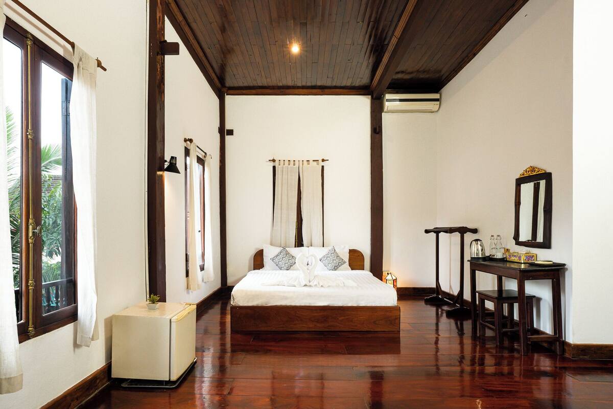 A bedroom with a wooden bed, a bedside table with a mirror, and a small table with a lamp.