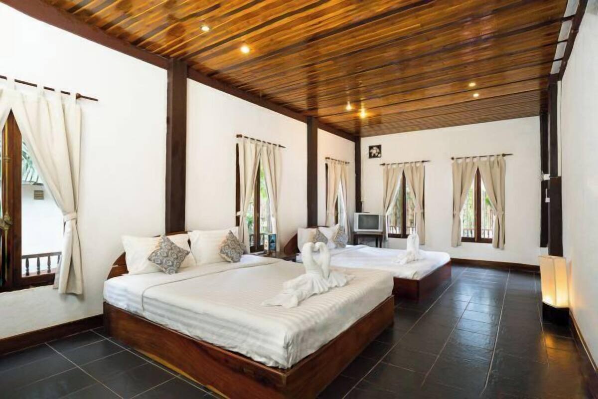 A hotel room with a large bed, a smaller bed, a TV, and a window with curtains.