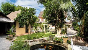 A serene courtyard with a small pond, lush greenery, and a pathway leading to a house. - Villa Khoum Xieng Thong Boutique (Luang Prabang)
