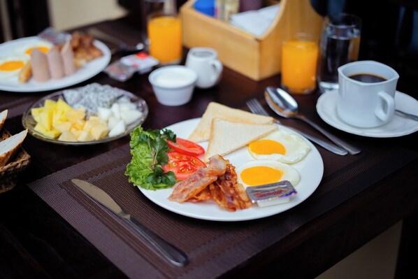 A breakfast setting with plates of eggs, bacon, toast, and fruit.