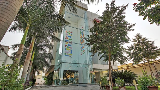 Un edificio moderno con fachada de vidrio, rodeado de palmeras y plantas en macetas.