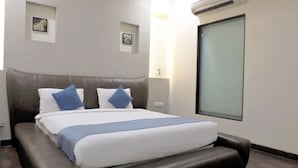 Una habitación de hotel con una cama grande, un cabecero, dos unidades de aire acondicionado fijadas a la pared y una ventana.