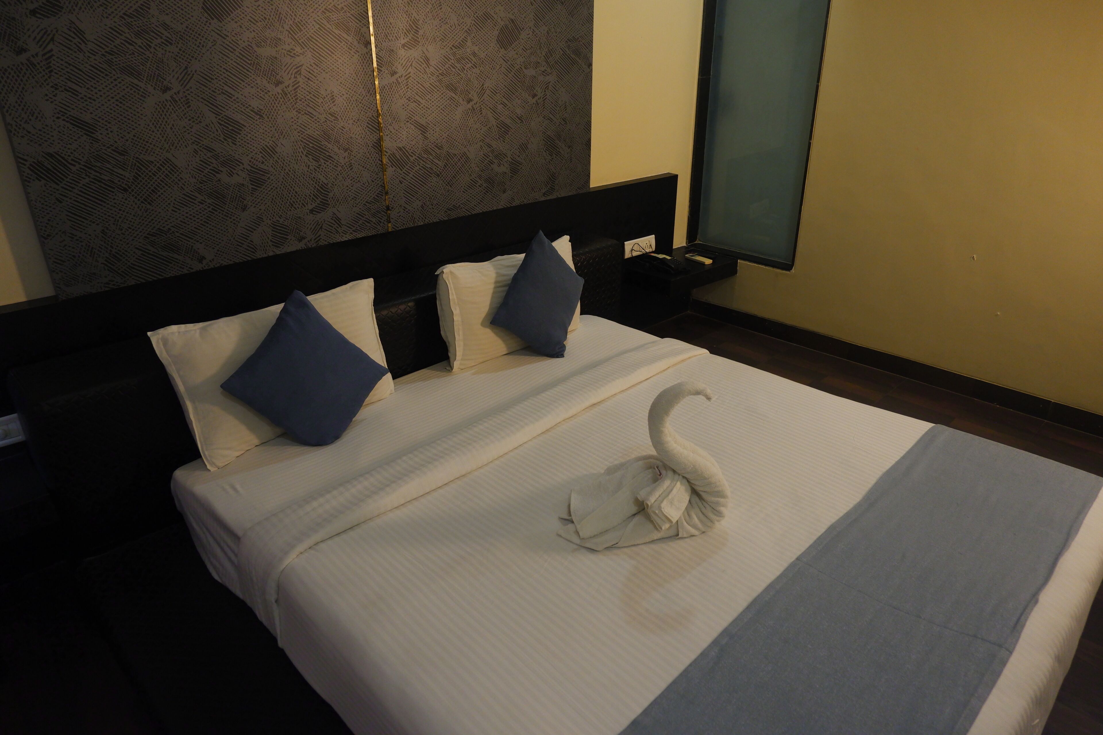 Una habitación de hotel con una cama bien hecha, un cabecero con diseño estampado y una pared con papel tapiz texturizado.