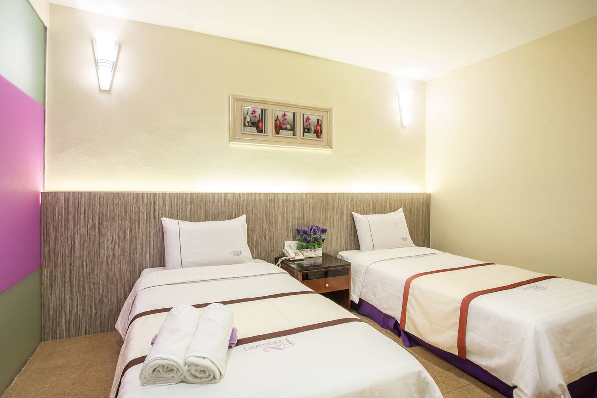 A hotel room with two beds, a nightstand, and a wall-mounted picture.