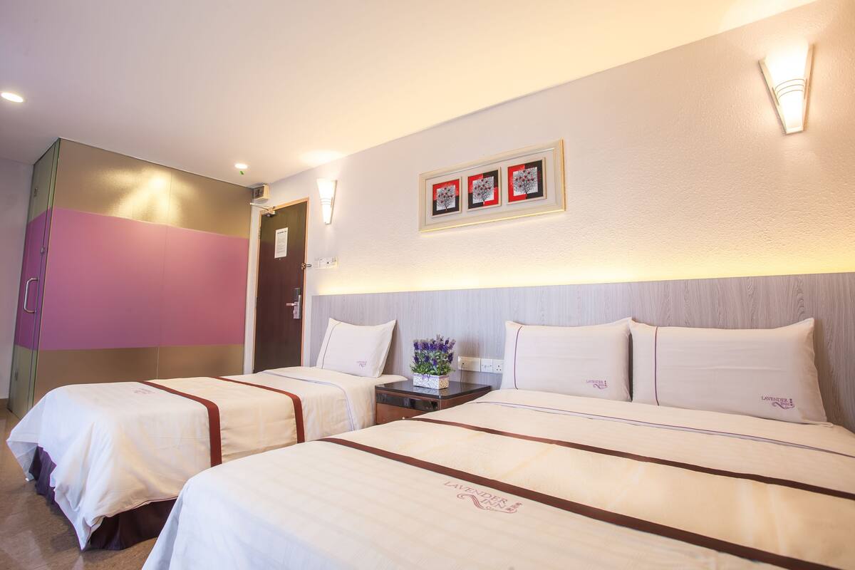 A hotel room with two beds, a nightstand, and a wall-mounted light fixture.