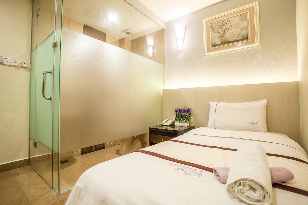 A hotel room with a bed, a nightstand, a telephone, and a glass shower enclosure.