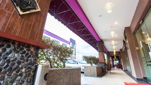 A hotel entrance with a stone facade, a covered walkway, and a parking area visible in the background. - Lavender Inn Nusa Bestari (Johor Bahru)
