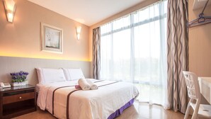 A hotel room with a bed, bedside table, lamp, and a view of the outdoors through the window. - Lavender Inn Nusa Bestari (Johor Bahru)
