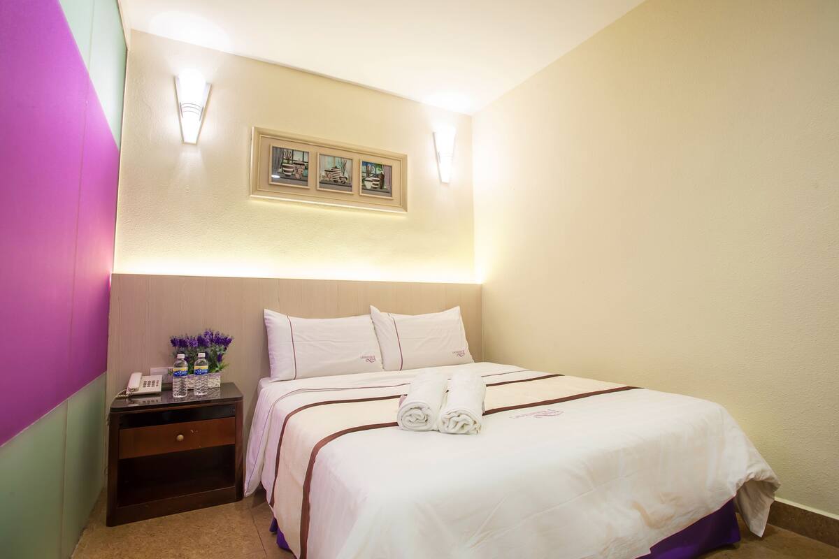 A hotel room with a bed, a nightstand, a phone, and a framed picture on the wall.