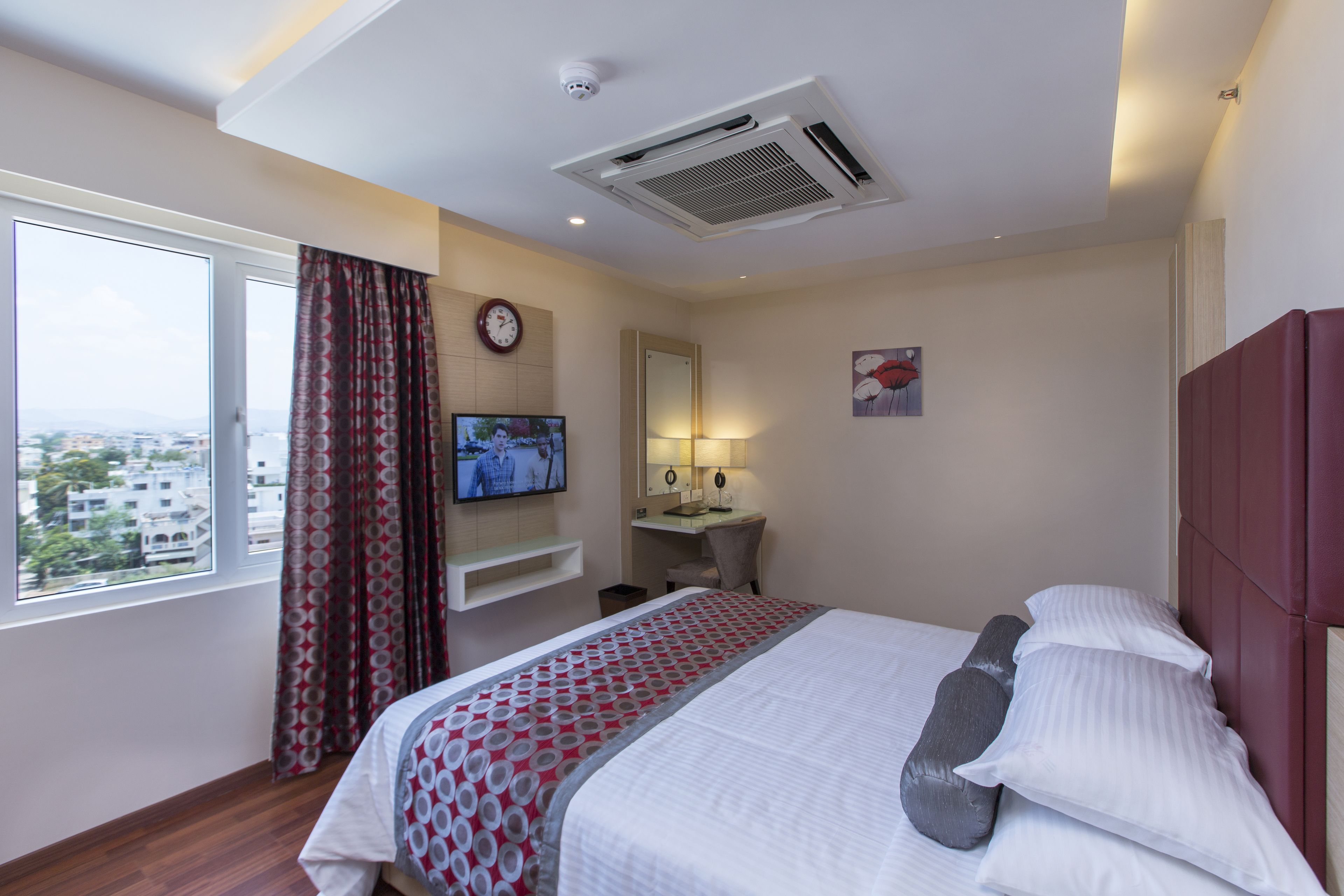 Camera d'albergo con un letto, una scrivania, una televisione, una finestra con tende e vista sulla città.