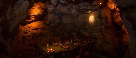 A cave dining area with tables and chairs, illuminated by small lights.