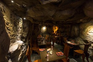 A restaurant with stone walls and carved figures, wooden tables and chairs, and a warm, dimly lit ambiance.