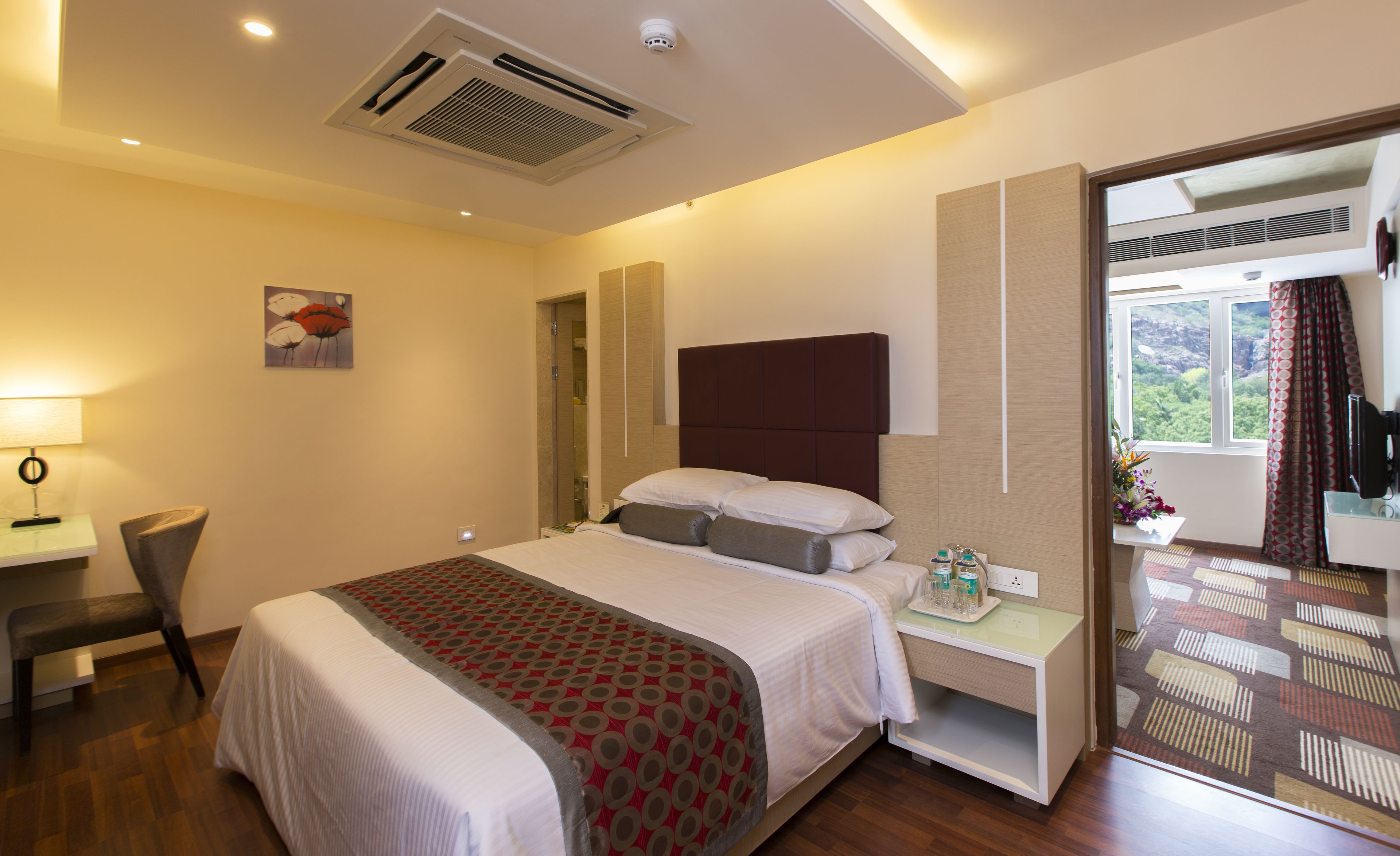 A hotel room with a large bed, bedside table, and a desk with a chair.