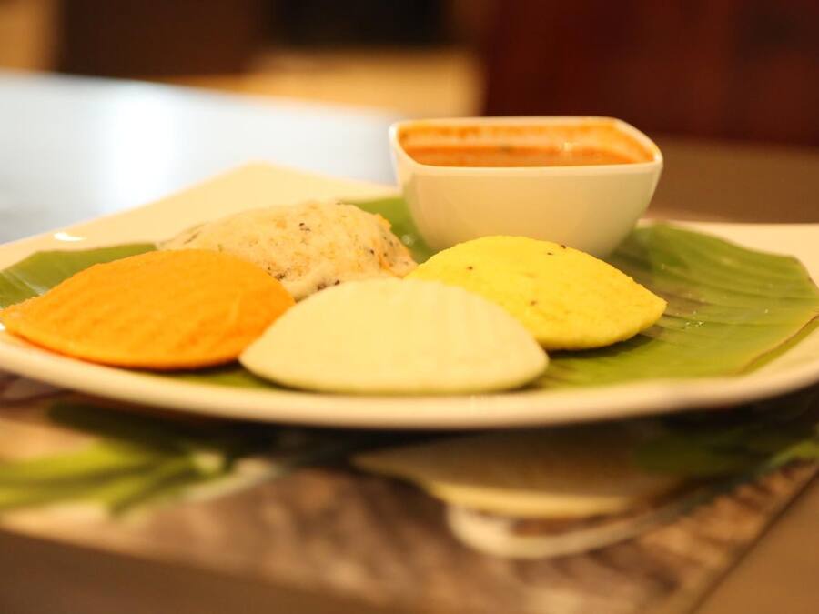 A plate with four different colored food items and a small bowl of sauce on a leaf.