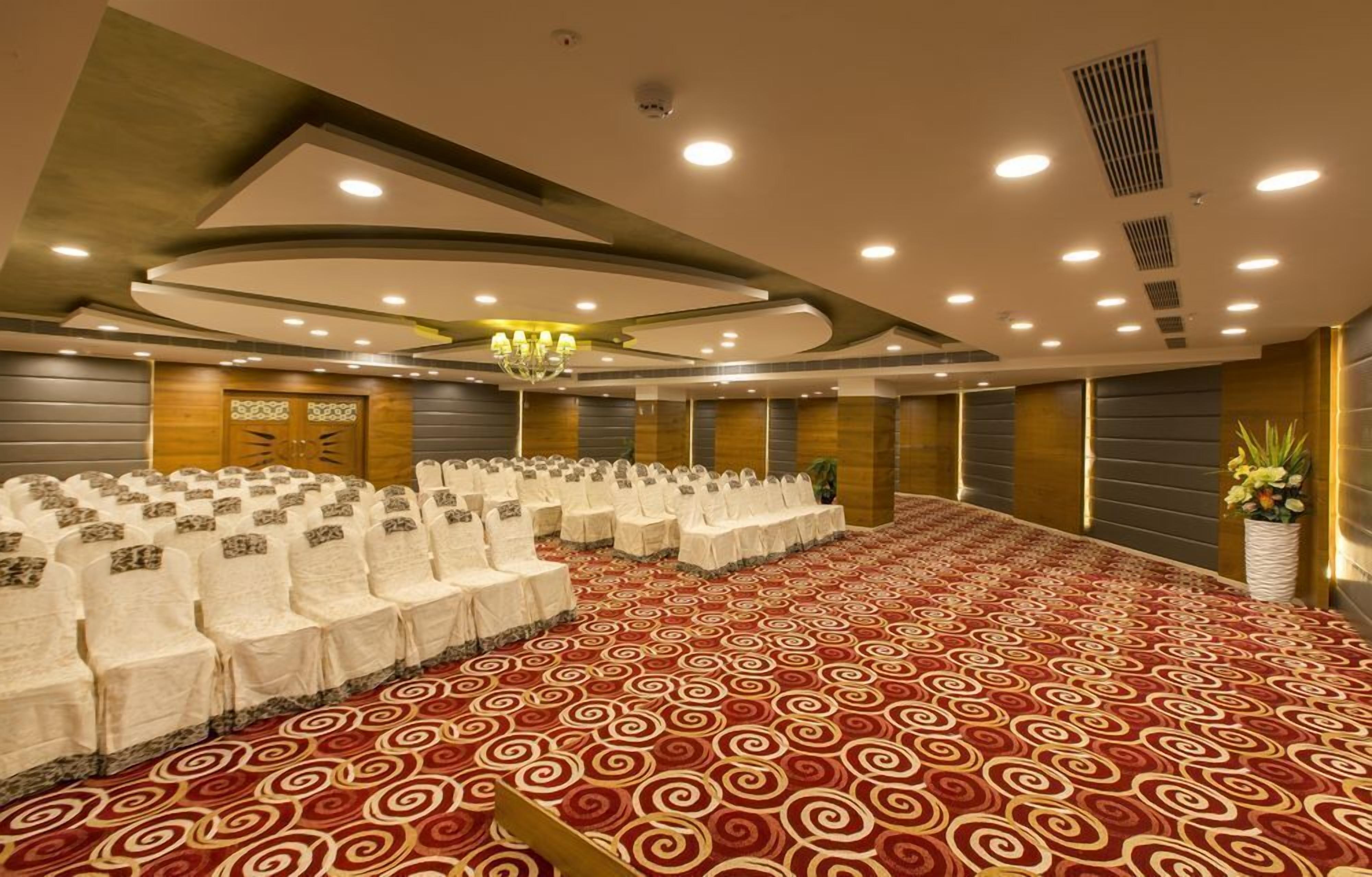 A conference room with rows of white chairs, a red patterned carpet, and a chandelier.