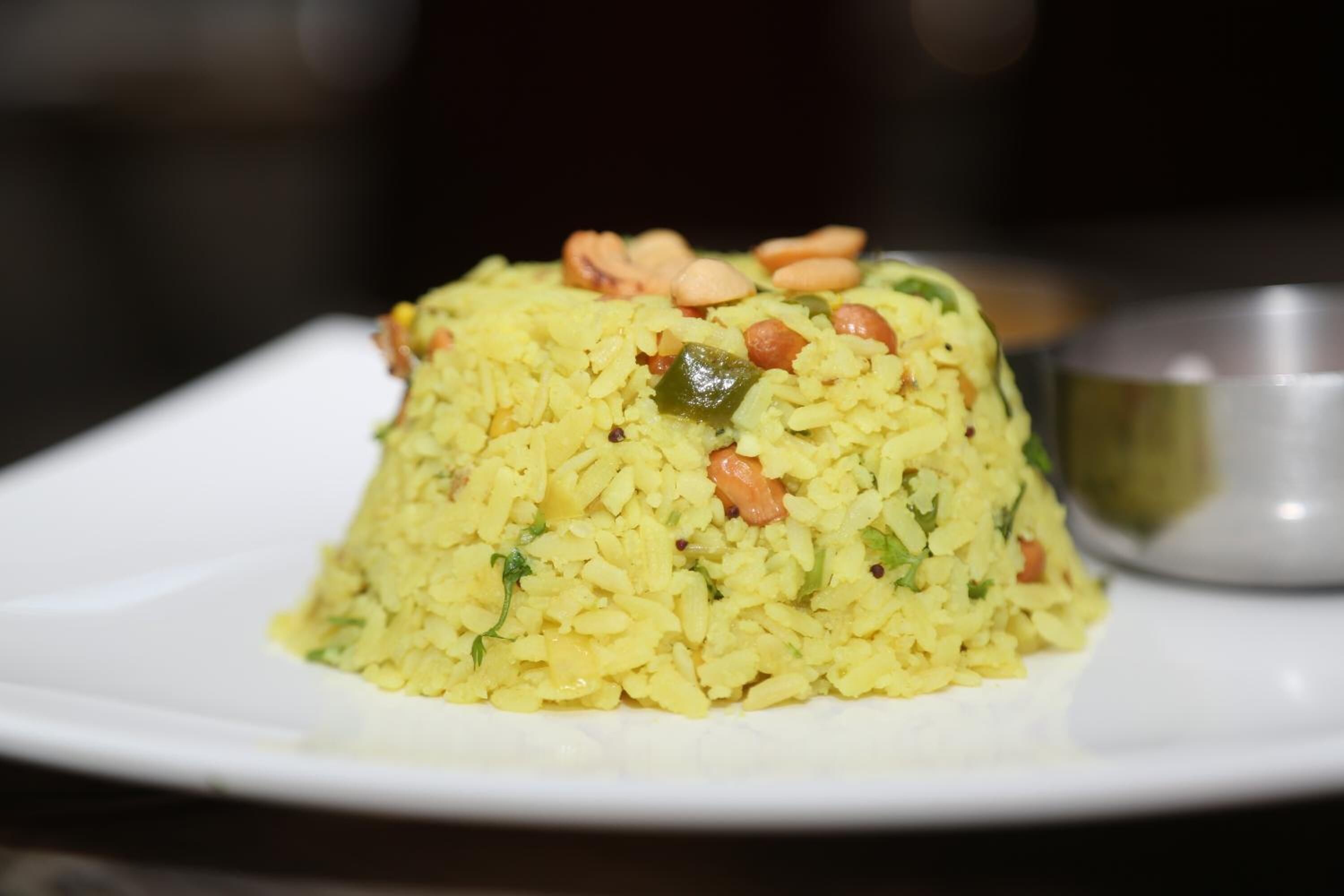 A dish of yellow rice with green peas and peanuts on a white plate.