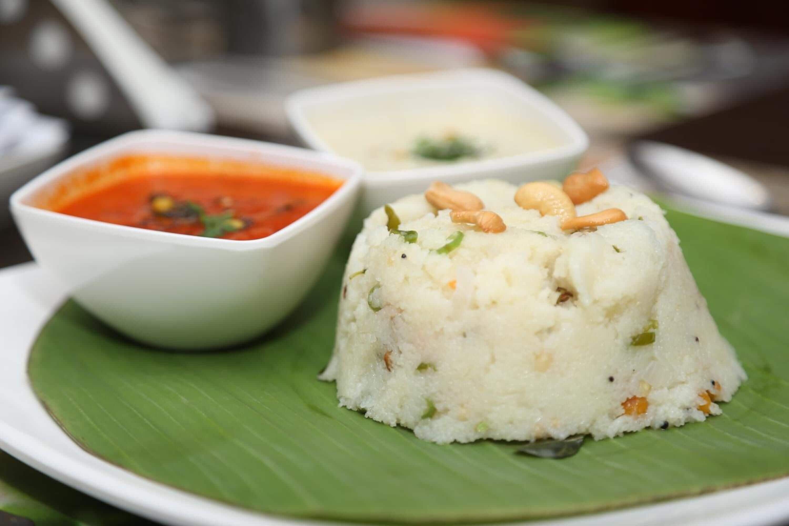 A dish of rice pudding with nuts on a banana leaf, accompanied by two small bowls of sauce.