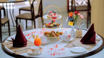 A round dining table with a tiered dessert stand, a vase of flowers, a teapot, and a glass of orange juice.