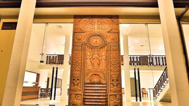 Una entrada con un panel de madera decorativo, un camino de adoquines y una puerta de cristal que da a una escalera.