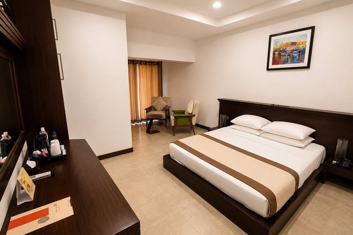 A hotel room with a bed, a desk with a tray of toiletries, a chair, and a painting on the wall.