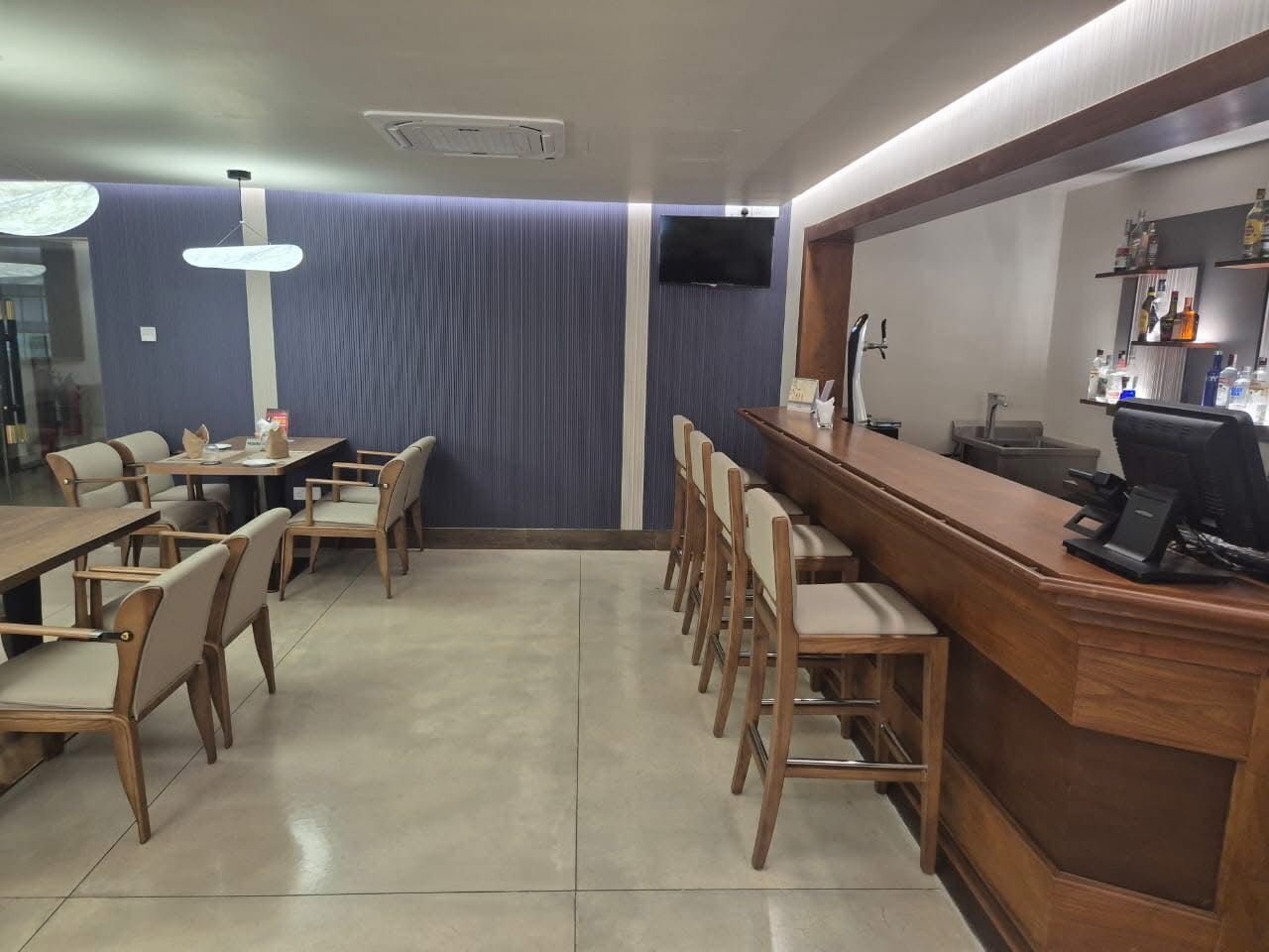 A restaurant with wooden tables and chairs, a bar area, and a television mounted on the wall.
