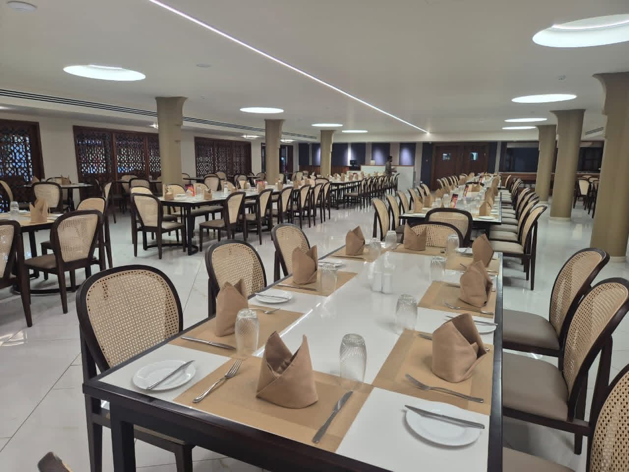 A large dining hall with multiple tables, chairs, and a high ceiling with recessed lighting.