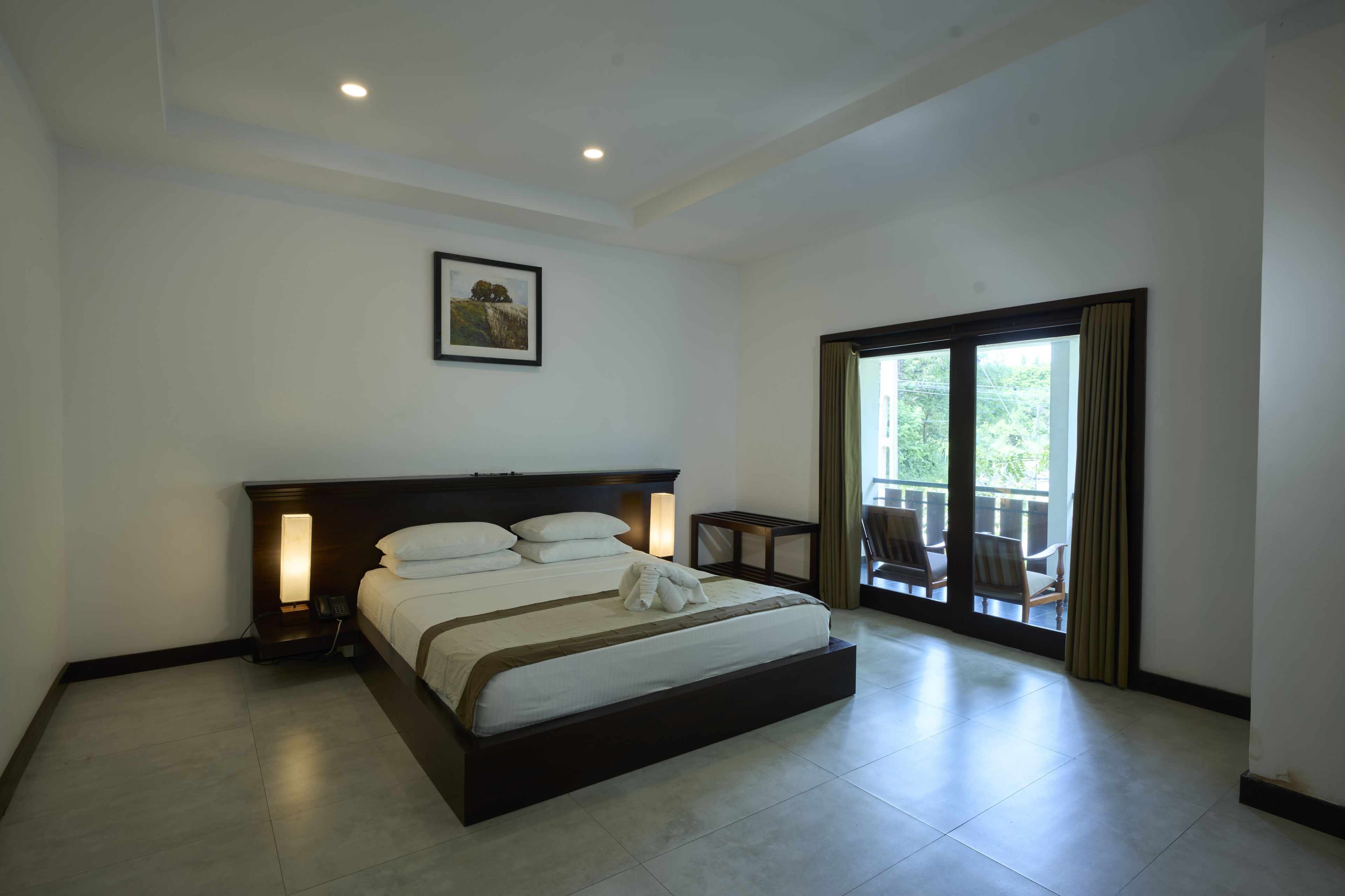A hotel room with a large bed, bedside lamps, a framed picture on the wall, and a view of the outdoors through a sliding door.