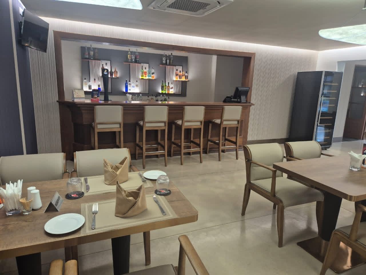 A restaurant with wooden tables and chairs, a bar area with shelves of bottles, and a modern interior design.