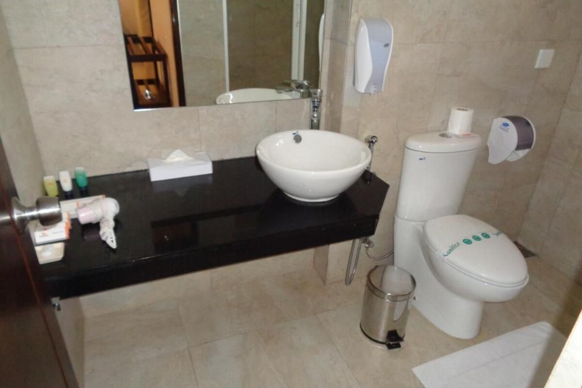 A bathroom with a black countertop, white sink, toilet, and a hand dryer.