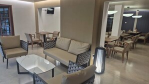 Un área de estar moderna con un sofá, sillas, una mesa de centro y una zona de comedor con mesas y sillas.