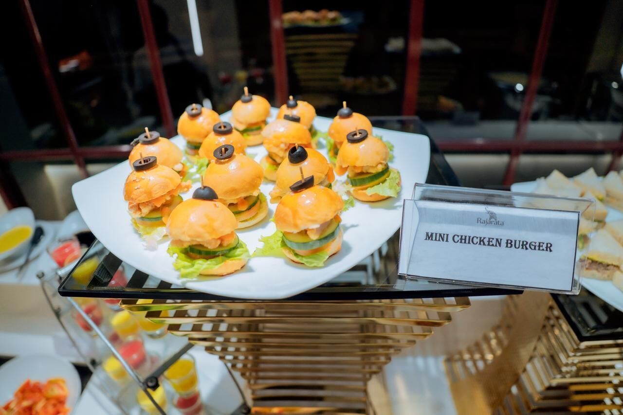 A buffet table with a plate of mini chicken burgers and a sign indicating the dish.