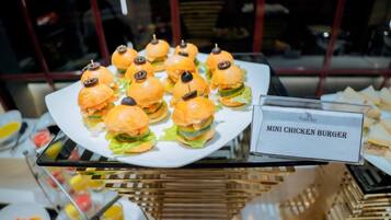 A buffet table with a plate of mini chicken burgers and a sign indicating the dish.