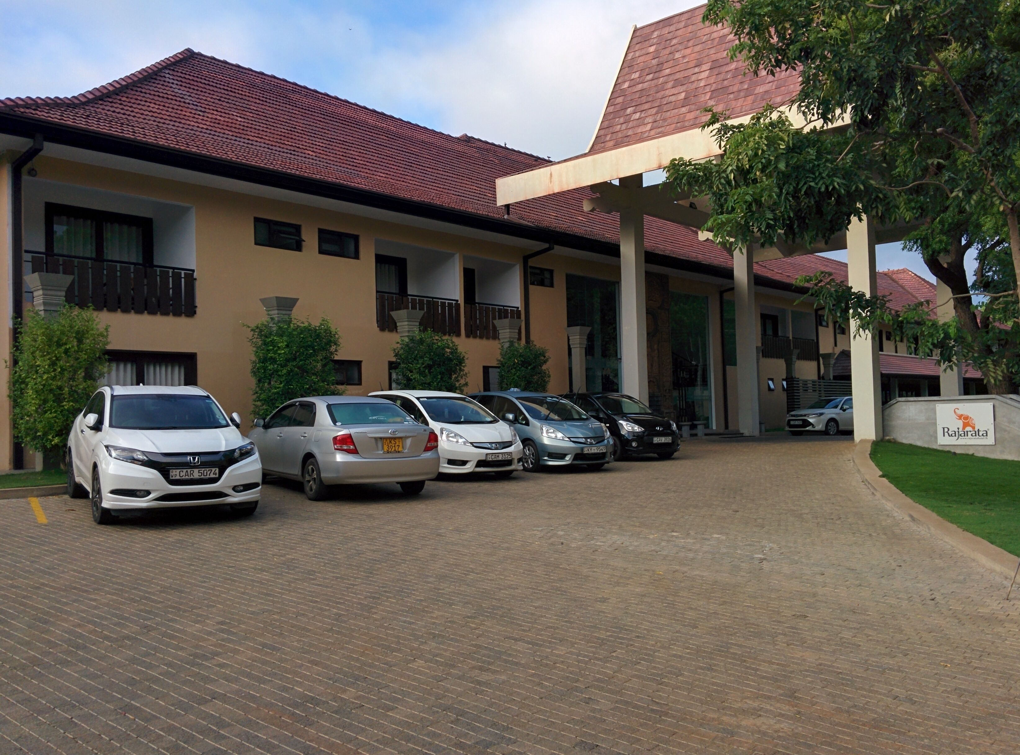 A building with a tiled roof and multiple windows. There are several cars parked in front of the building.