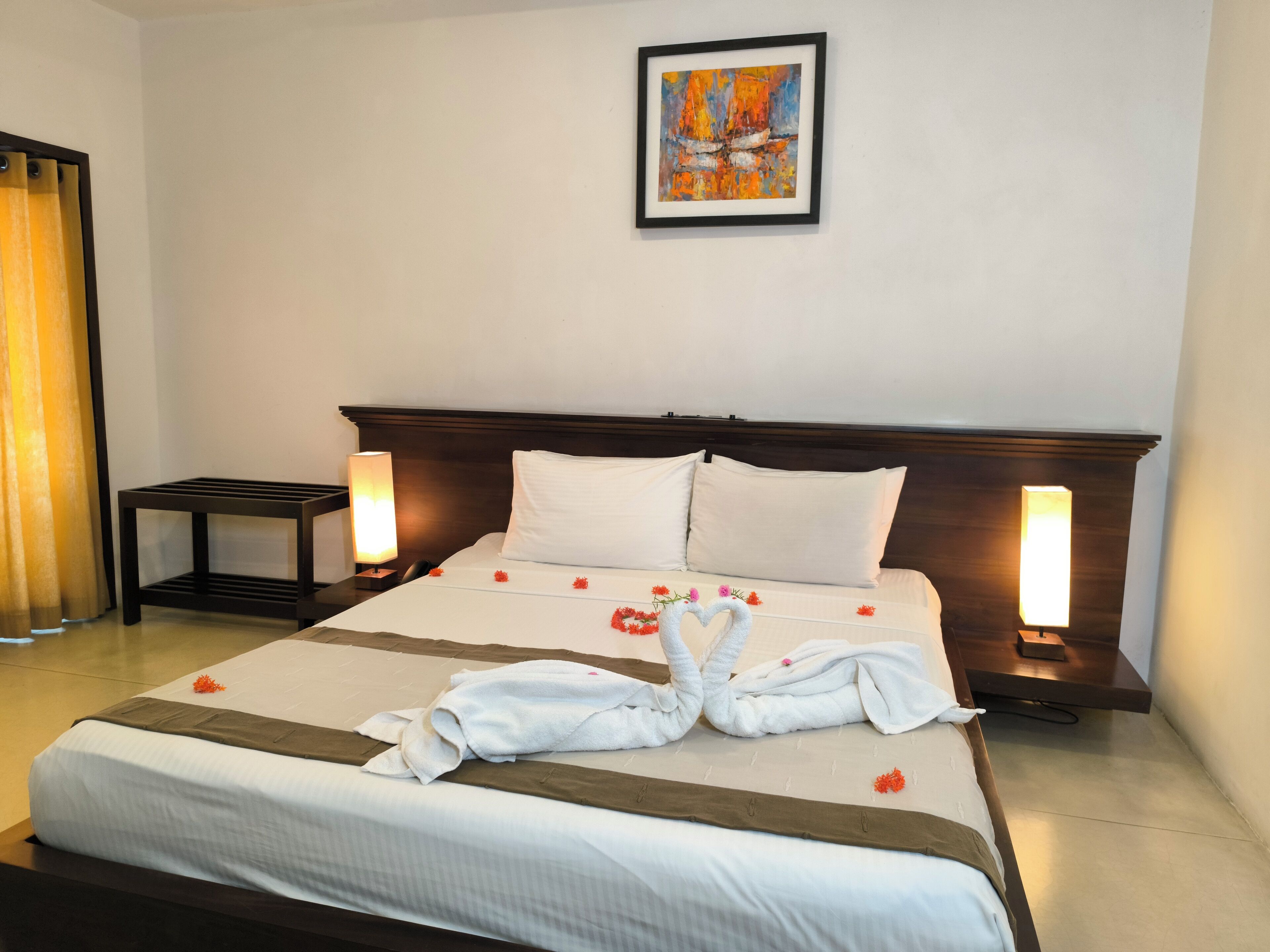 Una cama bien hecha con una escultura de toallas, dos lámparas de noche y un cuadro en la pared.
