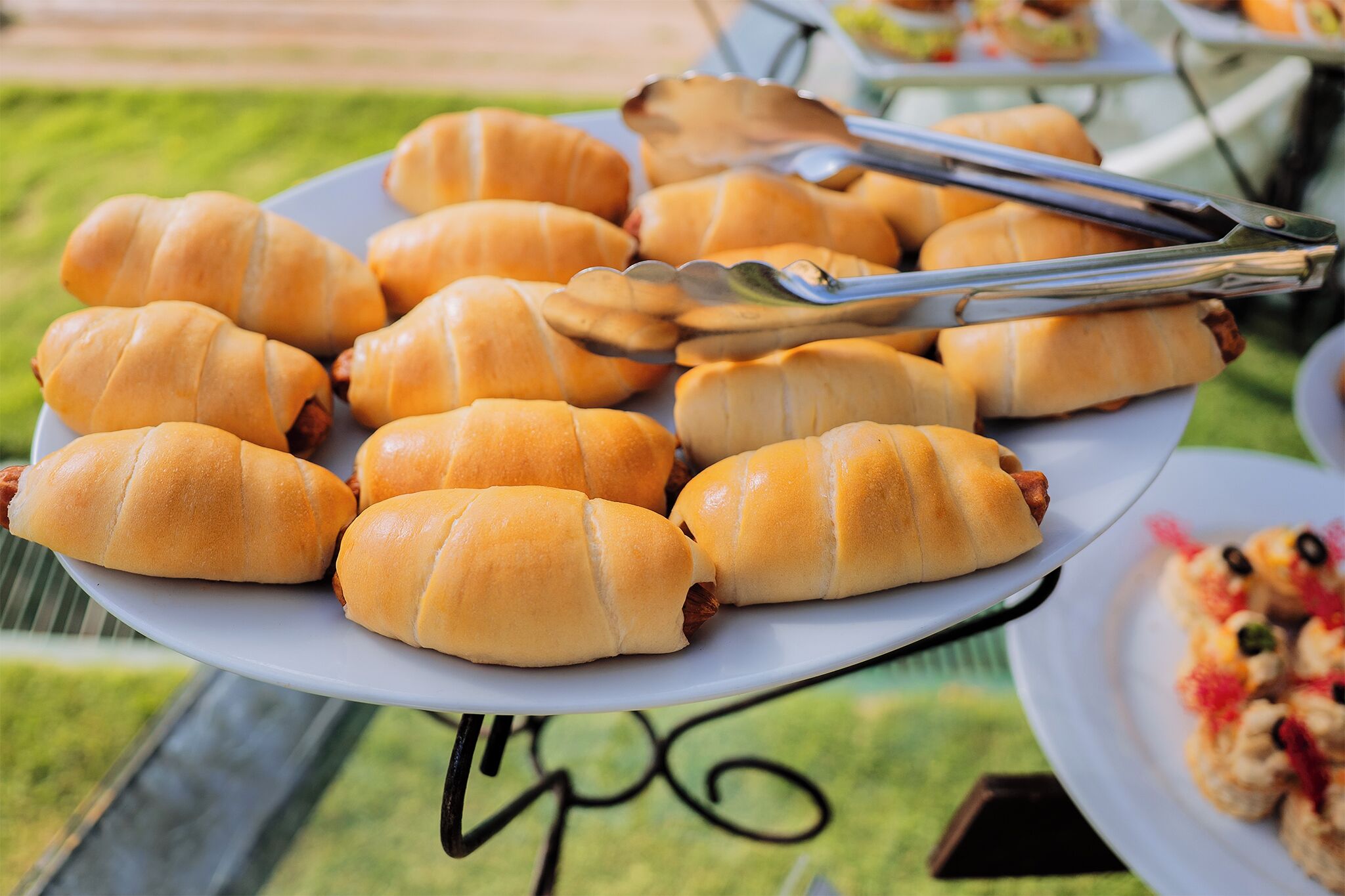 A plate of hot dogs on a white plate with a pair of tongs.