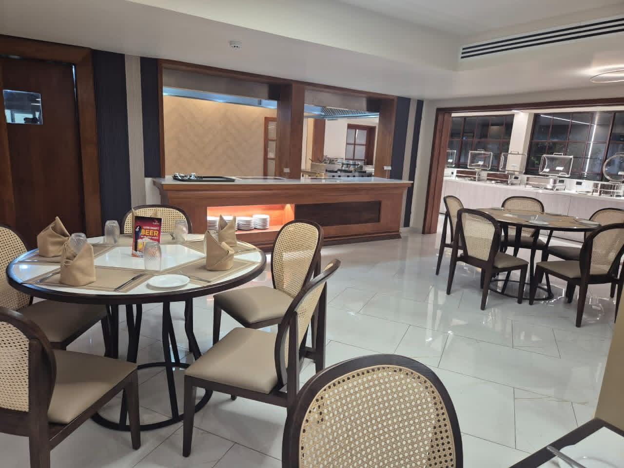 Un comedor de hotel con mesas redondas, sillas acolchadas y un mostrador tipo buffet.