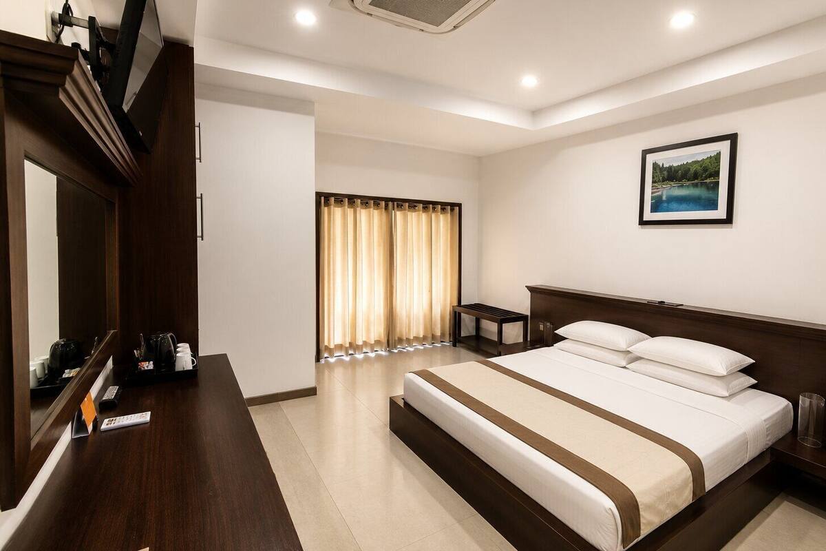 A hotel room with a bed, a desk with a mirror, a television, and a framed picture on the wall.