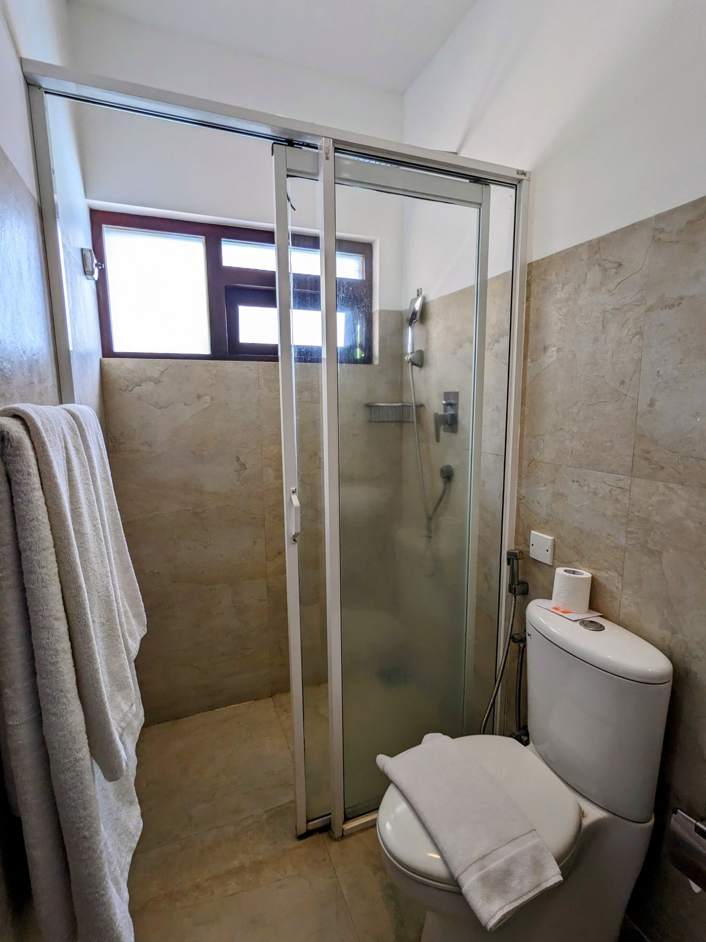 Un baño con ducha de mampara de vidrio, inodoro y perchero para toallas.