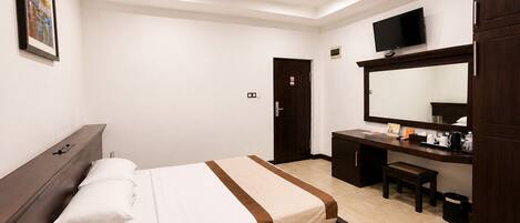 A hotel room with a bed, a desk, a TV, and a large mirror.