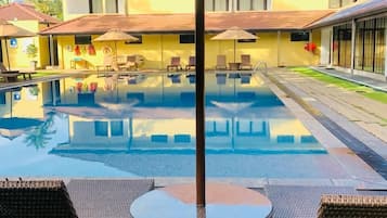 Una piscina con sillas de descanso y sombrillas, rodeada de edificios.