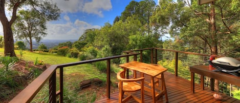 Una terraza de madera con una mesa y una silla, rodeada de exuberante vegetación y árboles.